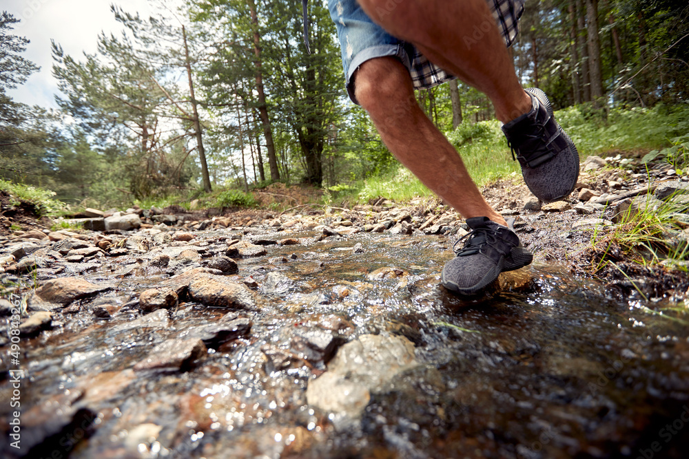 A young man is crossing a creek while hiking. Hiking, nature, relationship, together A young man is crossing a creek while hiking. Hiking, nature, relationship, together