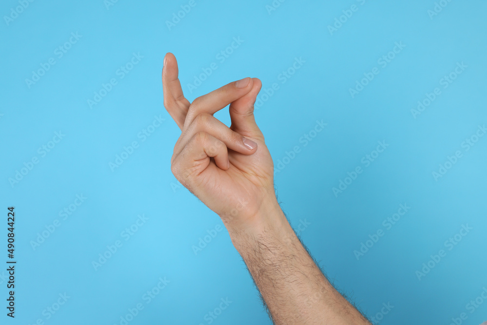 Man snapping fingers on light blue background, closeup of hand