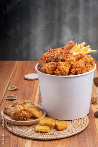 Fried chicken and french fries in paper bucket on wooden background, Deep fry Chicken and nuggets on wooden table.