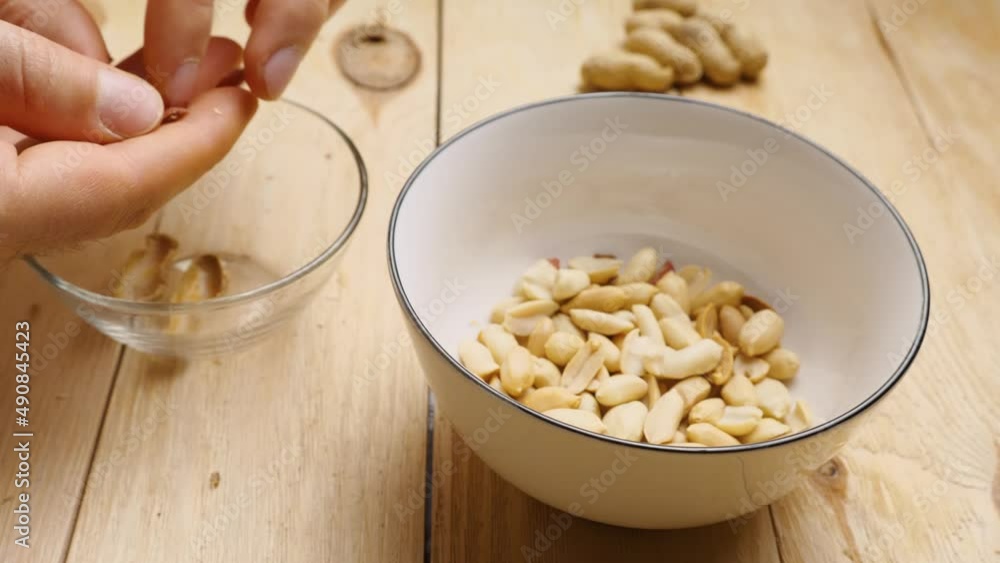 Close-up of a man's hands peeling roasted peanuts from their shells into a cup. Peeling an earthy peanut at home Close-up of a man's hands peeling roasted peanuts from their shells into a cup. Peeling an earthy peanut at home