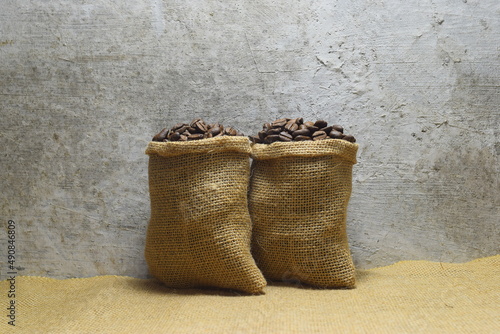 Close up photo of two burlap sacks containing roasted coffee beans against an old mossy wall as a background in a warehouse