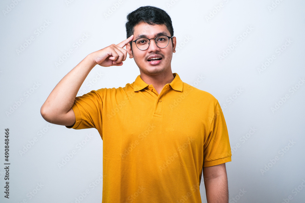Asian man smiling pointing to head with one finger, great idea or thought, good memory Asian man smiling pointing to head with one finger, great idea or thought, good memory