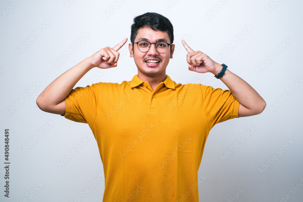 Asian man smiling pointing to head with one finger, great idea or thought, good memory Asian man smiling pointing to head with one finger, great idea or thought, good memory
