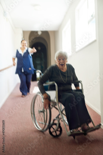 Im busting out of this joint. Shot of a mischievous senior woman using her wheelchair to run away form her nurse in an old age home. © Tamani Chithambo/peopleimages.com