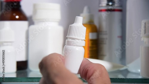 hand picking eye drops bottle from medicine cabinet photo
