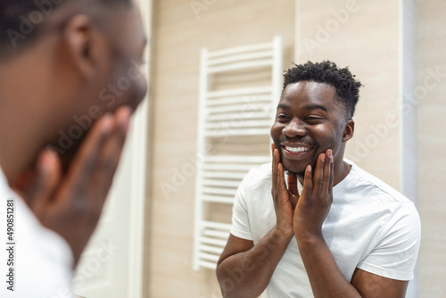 Morning hygiene  Handsome man in the bathroom looking in mirror. Reflection of Africanman with beard looking at mirror and touching face in bathroom grooming