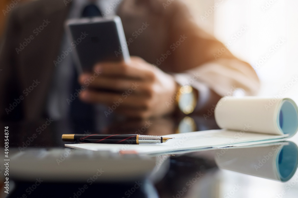 Business man hand using mobile smart phone with checkbook, pen and calculator on the table with reflection. Business man hand using mobile smart phone with checkbook, pen and calculator on the table with reflection.