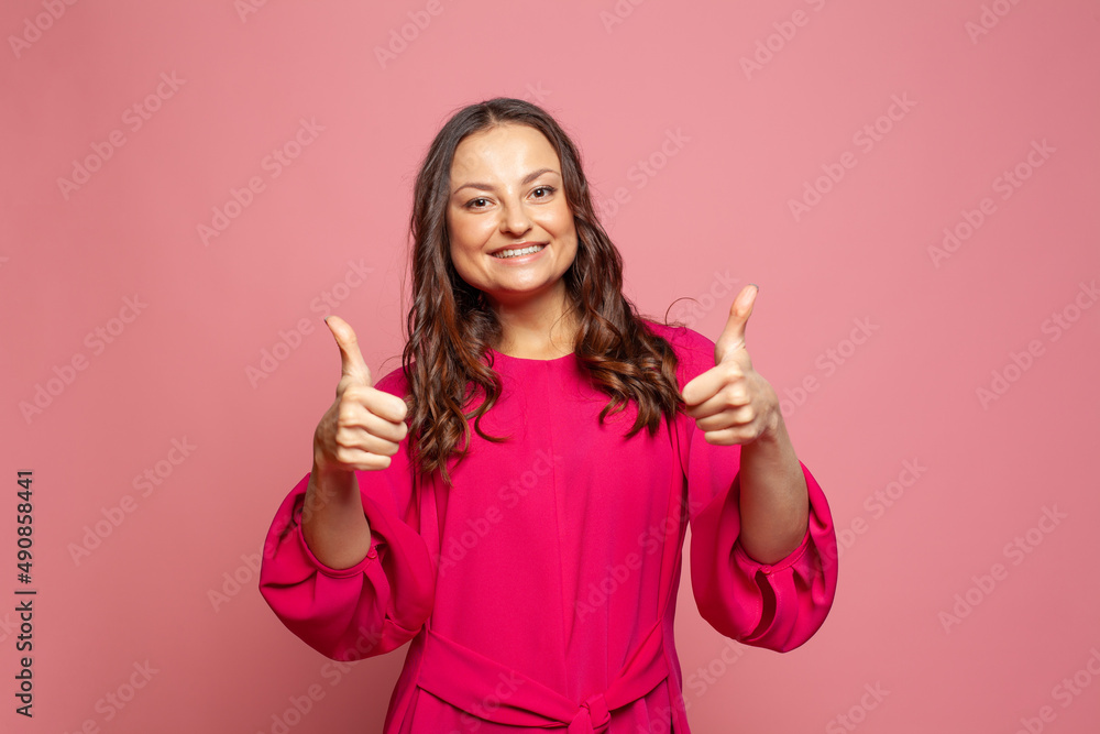 Young happy woman smiling showing thumbs up because something good has happened over pink background Young happy woman smiling showing thumbs up because something good has happened over pink background