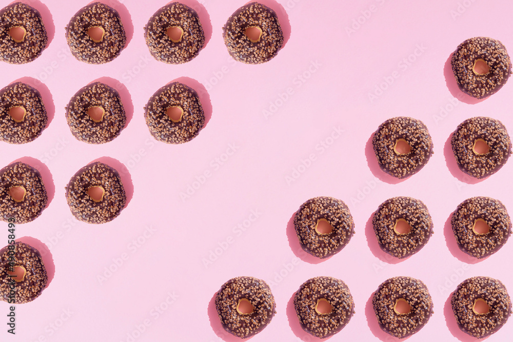 Arranged ring donuts like triangle with chocolate glaze and small crumbs on a pink pastel background. Minimal design and copy space.