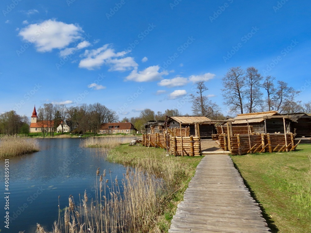 Araishi lake wooden fort and church on the other side of water, on a sunny spring day. Latvia, Gauja National Park in Cesis region. Araishi lake wooden fort and church on the other side of water, on a sunny spring day. Latvia, Gauja National Park in Cesis region.