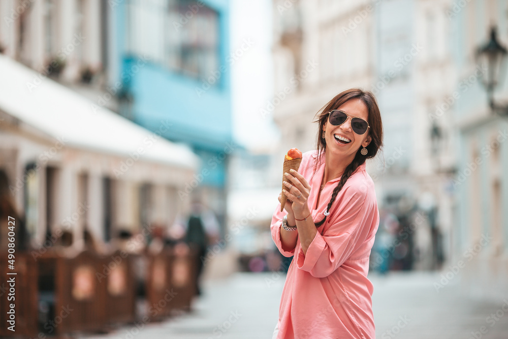 Happy young woman eating ice-cream on the street of european city.