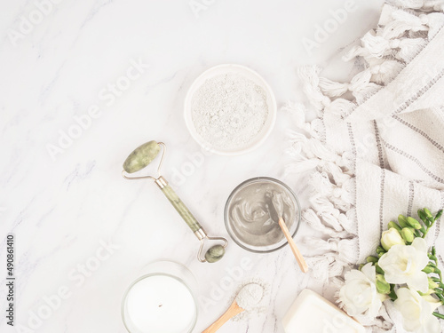 Organic blue clay for beauty facial mask., crystal massager, candle, cotton towel and white flowers on marble background.