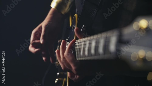 Male hands playing black electric guitar with golden mechanics filmed down the fretboard