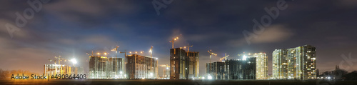 View of a large construction site with buildings under construction and multi-storey residential homes.Tower cranes in action on night sky background. Panoramic view.