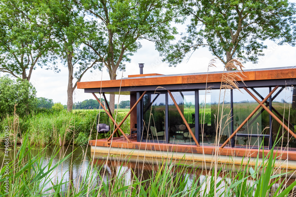 New modern house boat industrial style in canal between reed and trees in The Netherlands