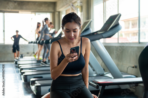 Asian athletic woman using mobile phone for social media or online shopping while workout exercise at fitness gym. Healthy female do sport training at sport club. Health care motivation concept