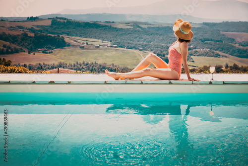 woman sitting by the pool with a cocktail  admiring green ladscape in Tuscany, Italy