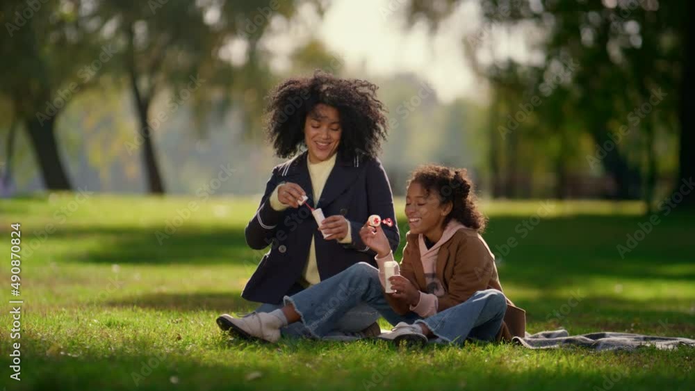 Happy daughter blowing soap bubble sitting in sunny park. Joyful family weekend. Happy daughter blowing soap bubble sitting in sunny park. Joyful family weekend.