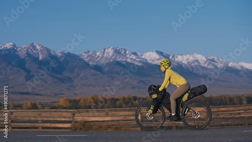 Fototapeta Naklejka Na Ścianę i Meble -  The woman travel on mixed terrain cycle touring with bikepacking. The traveler journey with bicycle bags. Sport tourism bikepacking, bike, sportswear in green black colors. Mountain snow capped.