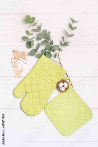 Fresh green plant, oven mitt and potholder on white wooden table. Easter mockup, kitchen accessory. Cooking mitten, oven-glove. Flat lay with copy space photo