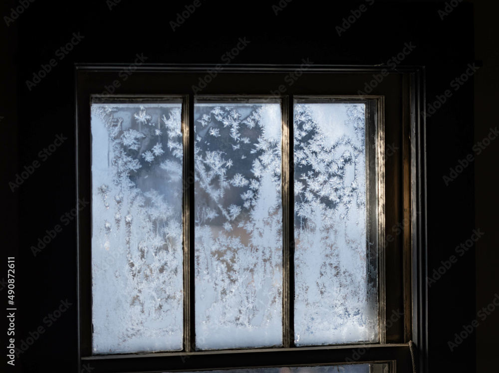 Old fashion window covered in frost with morning light shining thru the glass, dark contrast inside, shadows and light. Old fashion window covered in frost with morning light shining thru the glass, dark contrast inside, shadows and light.