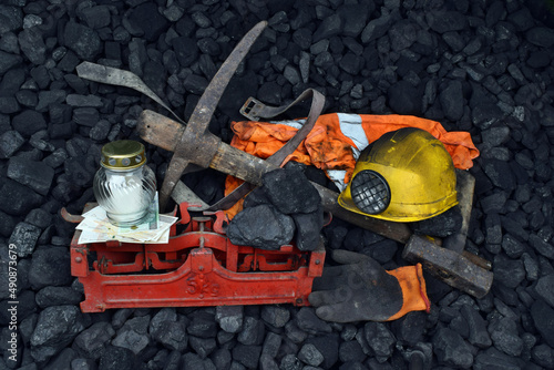 The miner belongings (helmet, gloves, pickaxe, vest, belt), graveyard candle and coal on the weight as concept after the fatal accident