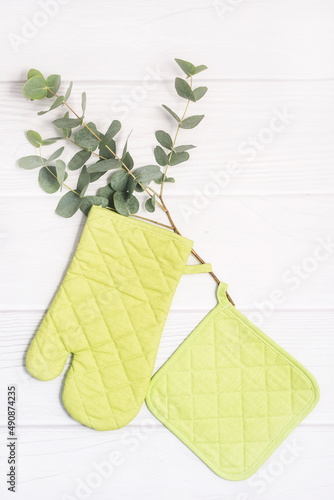 Fresh green plant, oven mitt and potholder on white wooden table. Kitchen accessory. Cooking mitten, oven-glove. Vertical flat lay photo.. photo