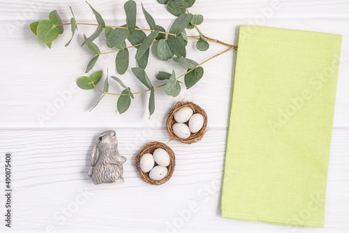 Flatlay composition with green linen kitchen towel or textile napkin. and Eucalyptus twig on white wood table. Copy space for text. Easter rustic farmhouse mockup.