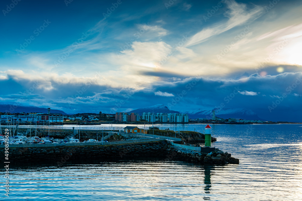 Hafeneinfahrt von Bodø mit Leuchtfeuer und Jachthafen, Segelschiffe und Hochhausquartier im Abendlicht. Halo in der Wolke. Abend in Norwegen mit Schiffleitsystem