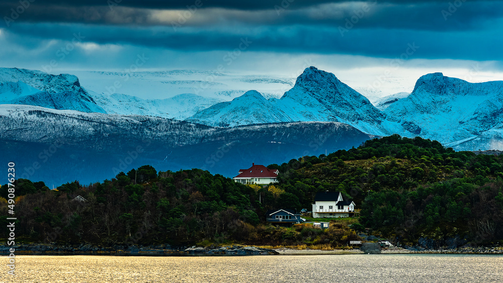 kleines Dorf an der norwegischen Küste in der Gegend von Tonnes, mit schneebedeckten Bergen im Hintergrund und Swartisen Gletscher, in Wolken gehüllt. Landschaft Norwegen Nordland
