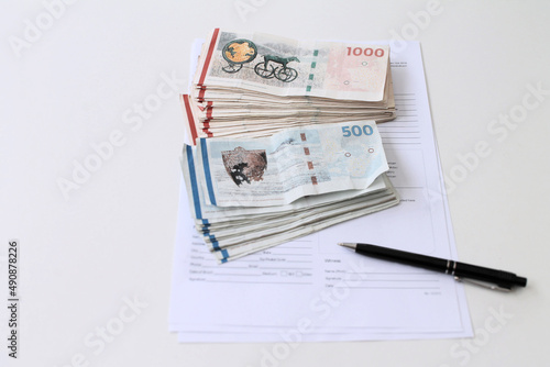 Two piles of Danish money kroner bills and a trade contract paper to sign with a pen