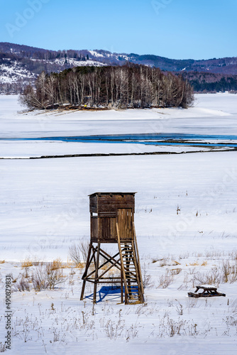 Winter landscape with a watch post and tributary River entering the frozen lake with with lake island and hills in the background background. Frozen Lake on a cold winter day.
 photo