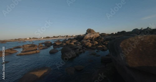 FPV drone above the sea and rocks next to a lighthouse at sunset
