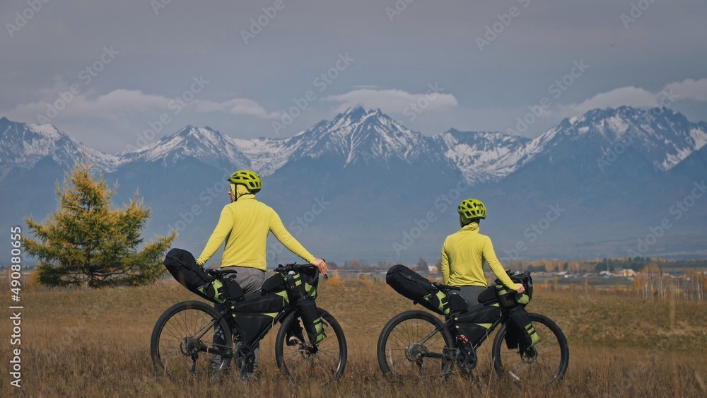 The man and woman travel on mixed terrain cycle touring with bikepacking. The love couple journey with tent in nature with bicycle bags. Stylish bikepacking, bike, sportswear in green black colors. The man and woman travel on mixed terrain cycle touring with bikepacking. The love couple journey with tent in nature with bicycle bags. Stylish bikepacking, bike, sportswear in green black colors.