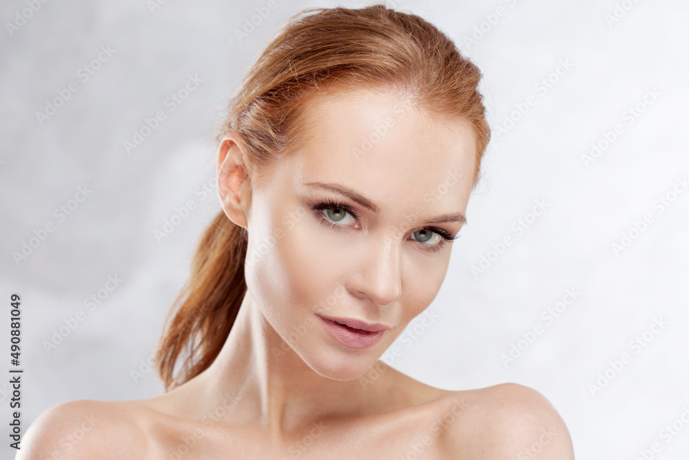Naklejka premium A young attractive red-haired woman with clear skin, a delicate portrait on a light gray background. Beauty and facial care