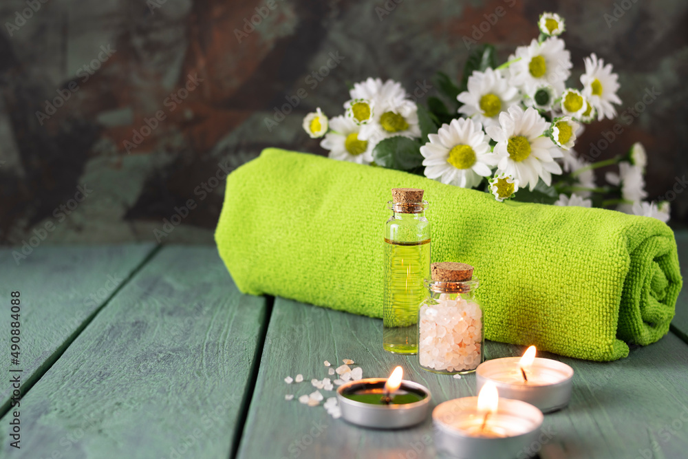 Bath salt, body oil and candles on green wooden boards. Green towel and daisies in the background. Massage kit. Space for text Bath salt, body oil and candles on green wooden boards. Green towel and daisies in the background. Massage kit. Space for text
