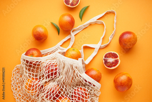 Sliced and whole blood oranges with sprigs of green leaves in an eco bag on a orange background. Top view.
