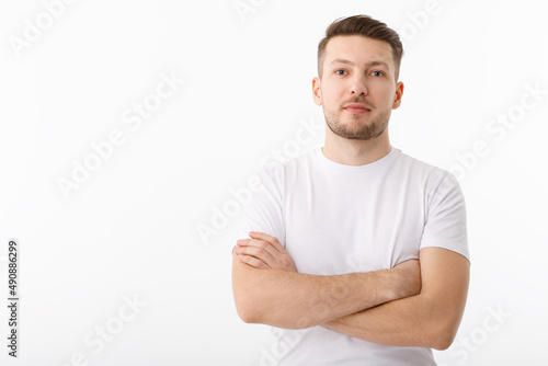 Portrait of a cheerful young man in a white T-shirt on a white background. The guy is standing looking at the camera and smiling.