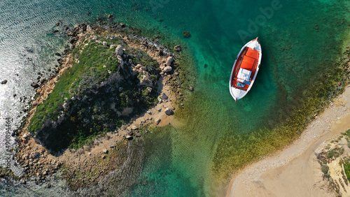 Aerial top view photo of red traditional wooden fishing boat anchored in Aegean island destination port with emerald sea