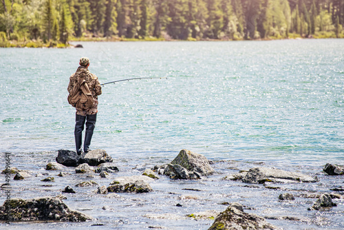 A man is fly fishing or spinning on a mountain lake. Recreational outdoor hobby and sport
