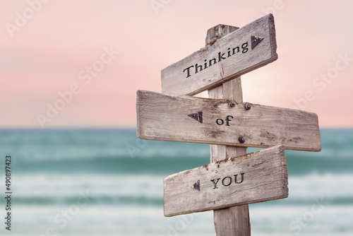 thinking of you text quote written on wooden signpost by the sea. Positive pink turqoise pastel theme.