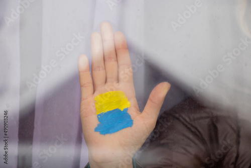 The hand of a girl in the window of her house with a painted yellow-blue flag of Ukraine, peace in Ukraine, stop the war, a protest action