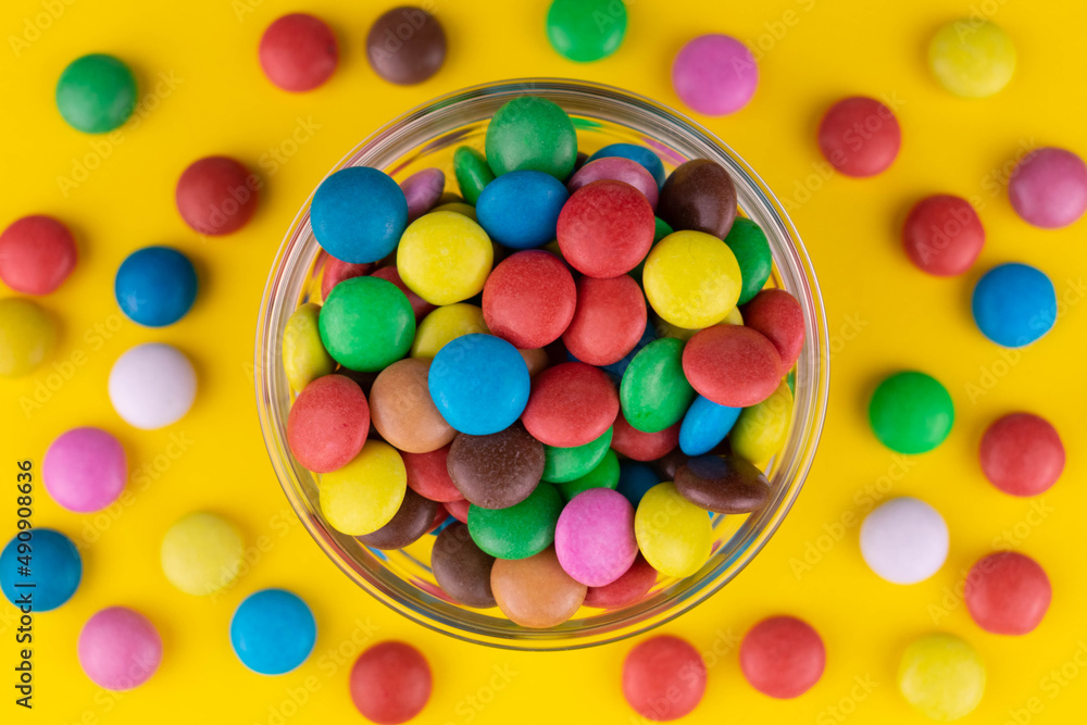 Small multi-colored sweets in a bowl on a yellow background.
