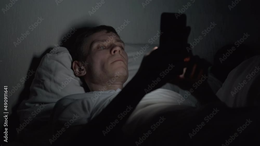 Young Man Lying in Bed and Using Smartphone at Late Night, News and Social Media Addiction. Insomnia and Sleep Disorder Concept Young Man Lying in Bed and Using Smartphone at Late Night, News and Social Media Addiction. Insomnia and Sleep Disorder Concept