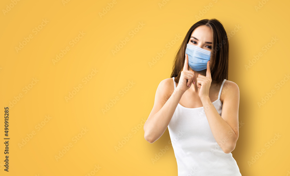 Coronavirus, covid-19, pandemic, protective concept - brunette happy smiling woman wearing showing face protection medical mask, orange yellow background. Copy space area for some sign text. Coronavirus, covid-19, pandemic, protective concept - brunette happy smiling woman wearing showing face protection medical mask, orange yellow background. Copy space area for some sign text.