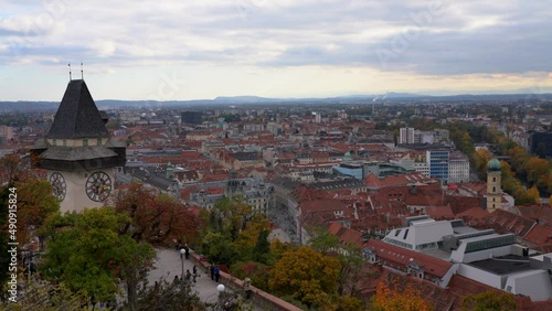 Aerial panorama view of Graz city old town from Schlossberg on a cloudy day in autumn, clock tower, art museum, city hall and colorful trees, Graz, Styria, Austria