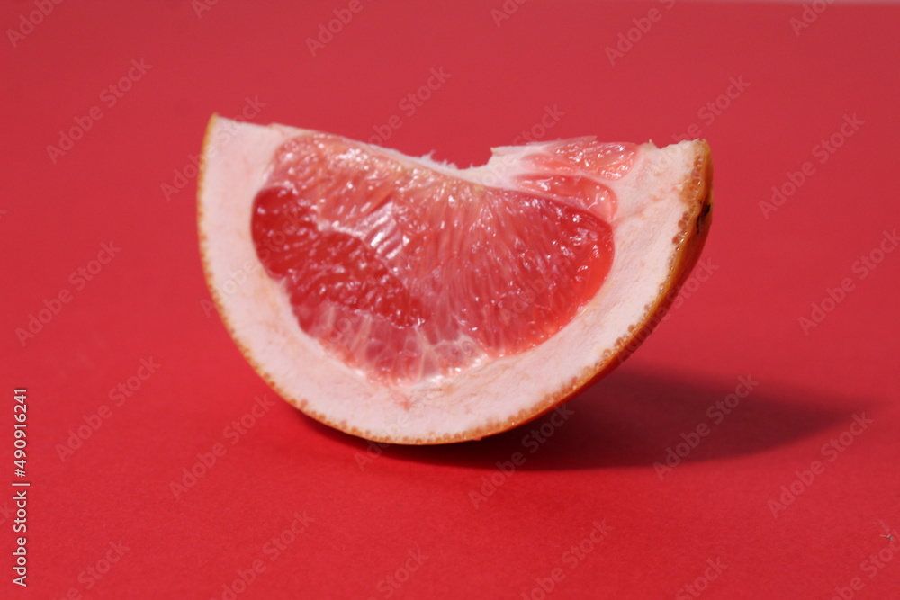a piece of a slice of red grapefruit on a red background with a hard shadow. Fruit creative benefit red on red
