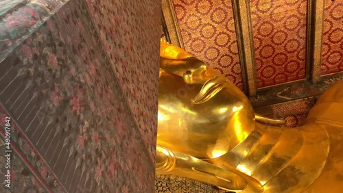 BANGKOK, THAILAND - Circa November, 2021: Golden Reclining Buddha Statue at Wat Pho, world heritage buddhist temple. This sleeping posture known as sihasaiyas. Beautiful background wall - Low angle  photo