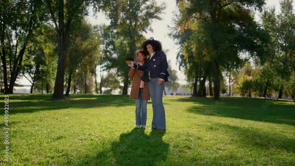 Smiling mom making online call waving at camera. Happy family posing in park. Smiling mom making online call waving at camera. Happy family posing in park.