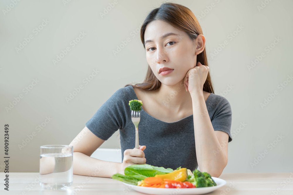 Diet in bored, unhappy beautiful asian young woman, girl on dieting, holding fork at broccoli in salad plate, dislike or tired with eat fresh vegetables. Nutrition of clean, healthy food good taste. Diet in bored, unhappy beautiful asian young woman, girl on dieting, holding fork at broccoli in salad plate, dislike or tired with eat fresh vegetables. Nutrition of clean, healthy food good taste.